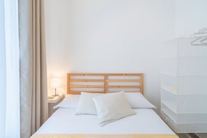 Un lit bien fait, avec une tête de lit en bois, une table de chevet avec une lampe et un meuble de rangement blanc doté d’étagères.