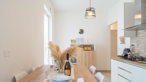 A modern kitchen with a wooden dining table, white chairs, a wine bottle, and pampas grass.