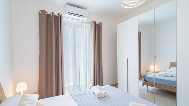 A hotel room with a bed, a bedside lamp, a mirror, and a window with curtains.