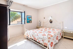 Una camera da letto con un letto, un comodino, una finestra che offre vista su una scala e un quadro appeso al muro.