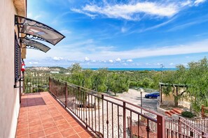 Un balcone con vista sul mare, un'auto parcheggiata all'esterno e un pergolato con piante rampicanti.