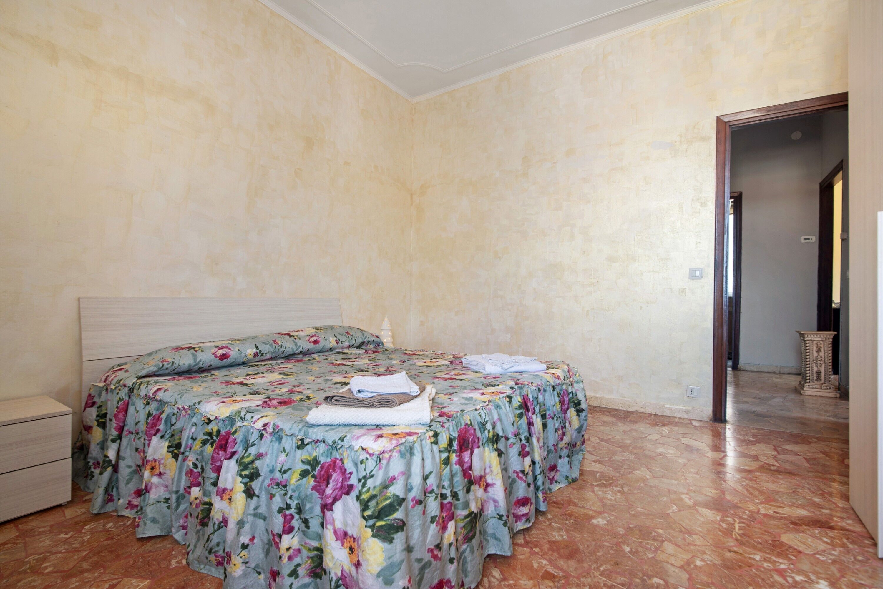 A bedroom with a bed, a nightstand, and a door leading to another room.