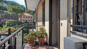 Ein Balkon mit Topfpflanzen, einem Metallgeländer und einem Gebäude mit rotem Dach im Hintergrund.
