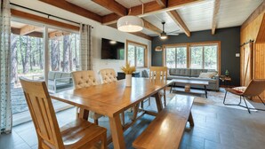 Un comedor espacioso con una mesa de madera y bancos, rodeado de amplios ventanales con vistas al bosque.