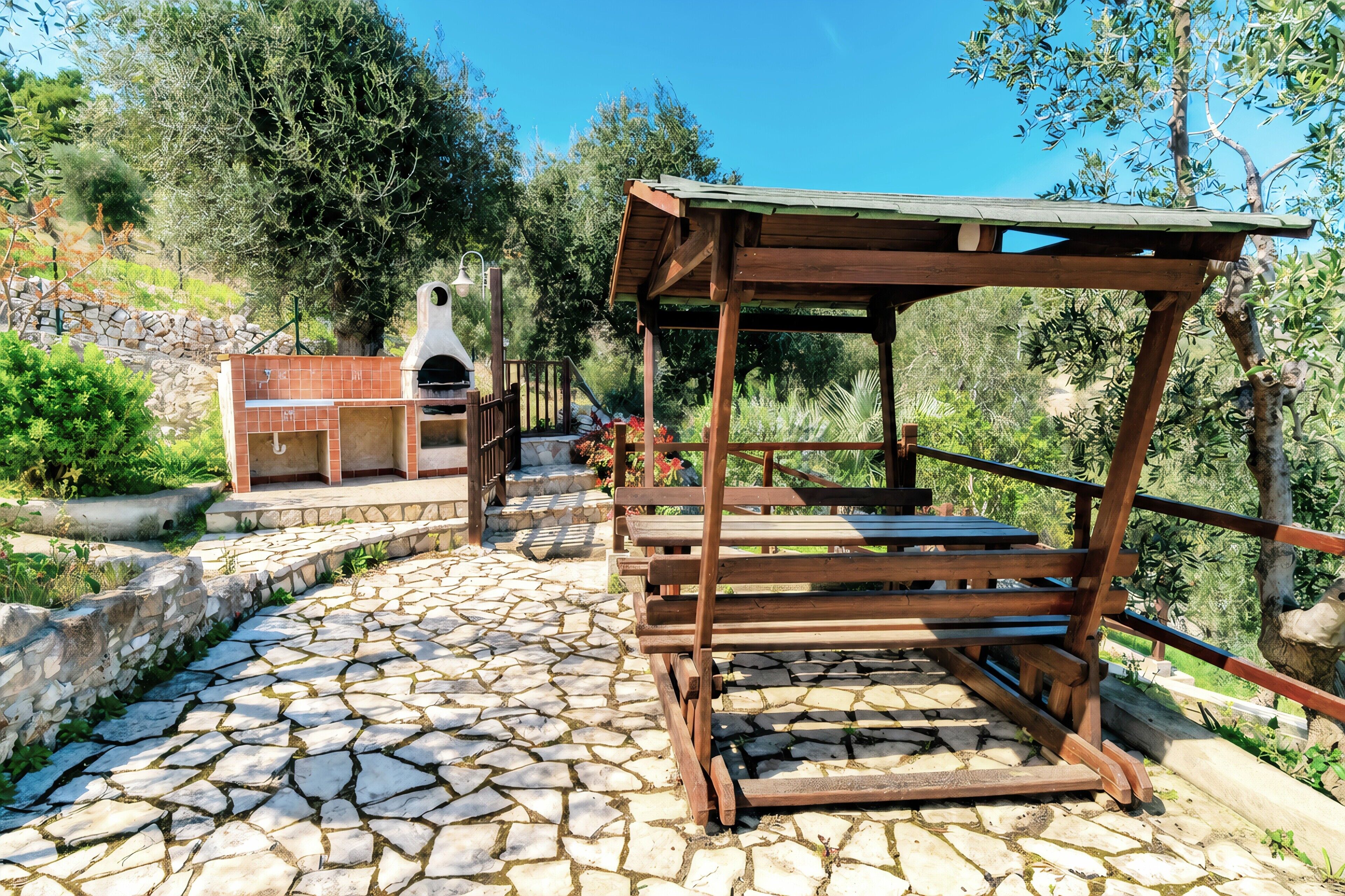 Een patio met stenen bestrating, een houten pergola en een barbecuehoek.