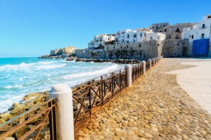 Un passeig marítim amb paviment de pedra, barana metàl·lica i edificis blancs amb balcons.