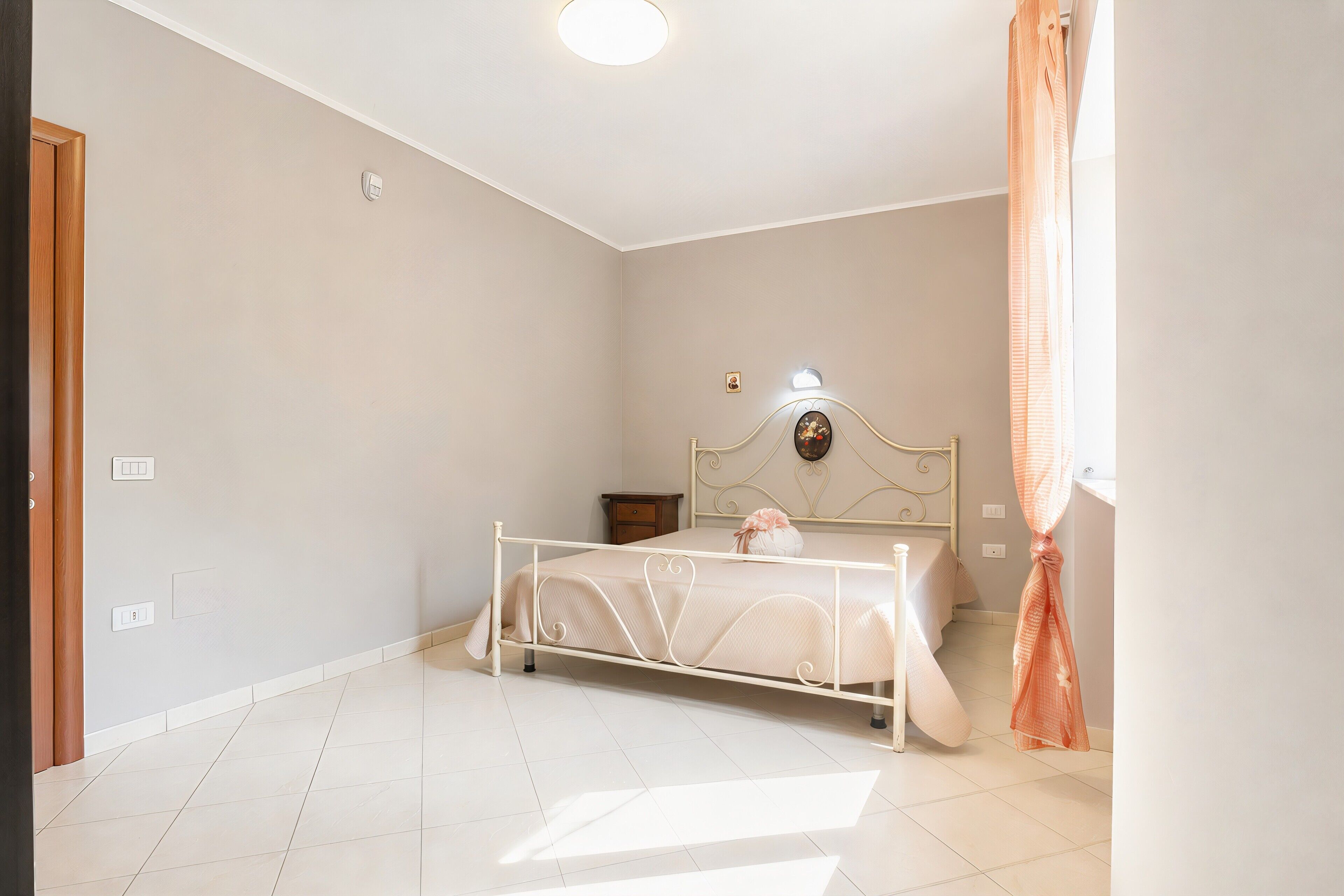 A bedroom with a bed, a nightstand, a wall clock, and a window with curtains.