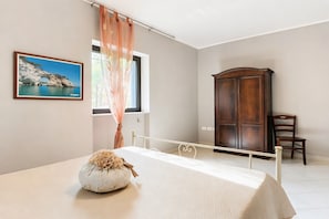 Un dormitori amb un llit, un armari de fusta, una cadira, una finestra amb cortines i un quadre encapçalat a la paret.