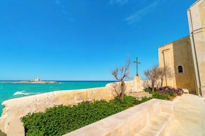 A coastal view with a lighthouse, a stone wall, and a building with a cross.