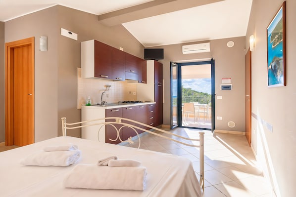 Una habitación de hotel con cama, baño, kitchenette y balcón con vistas.