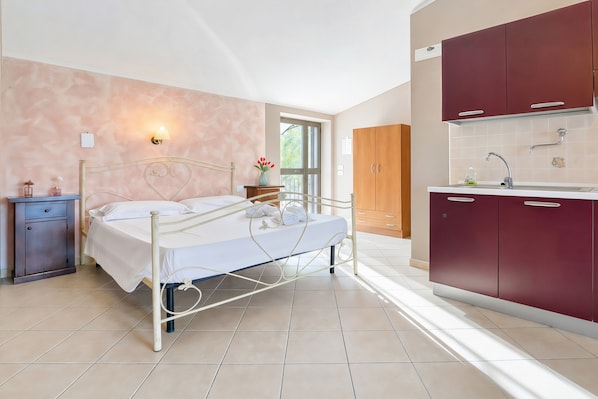 Ein Schlafzimmer mit Metallbettgestell, Nachttisch, Fenster und Blick ins Freie.