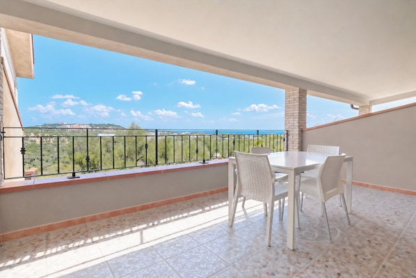 A balcony with a table and chairs, a view of the sea, and a tiled floor.