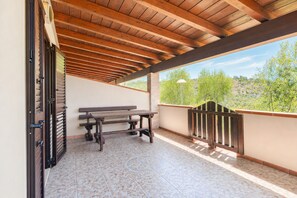 A covered outdoor area with a wooden bench and a table, a view of trees and hills, and a tiled floor. - Casa Mimosa at Villa Mapa: Sea View, Wi-Fi & Air Conditioning (Vieste)