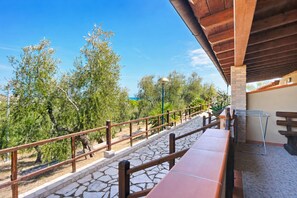 A terrace with stone flooring, wooden railings, and a view of trees.