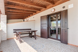 Un área de patio techada con un banco de madera y una puerta que da a un espacio interior.