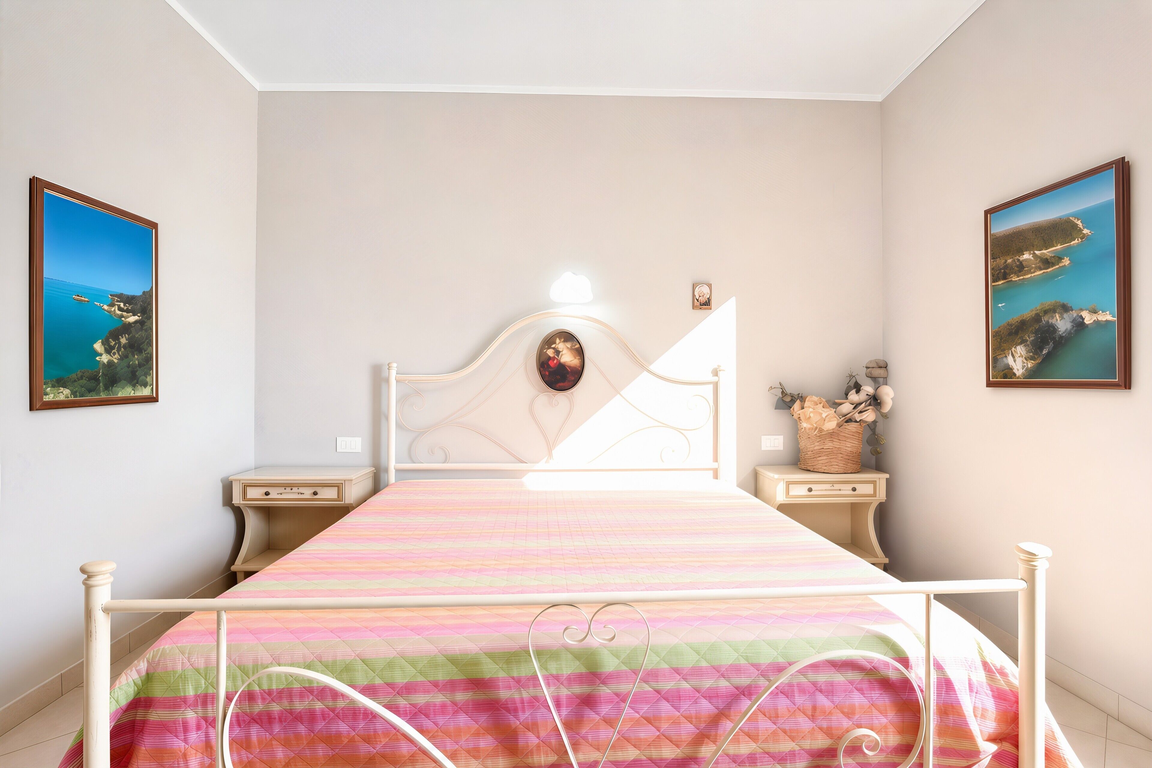 Un dormitorio con una cama, mesitas de noche, un cabecero y dos cuadros enmarcados en las paredes.