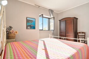 Un dormitorio con cama, ventana, armario de madera, una silla y un cuadro en la pared.