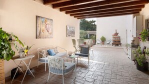An outdoor patio with a wooden ceiling, seating area with chairs and a sofa, a small table, and potted plants.