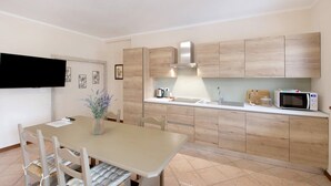 A modern kitchen with wooden cabinets, a dining table with chairs, a microwave, and a kettle.
