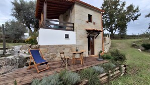 Una casa de piedra con una terraza de madera, una mesa pequeña y una silla.