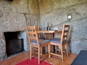Um quarto com paredes de pedra, lareira, cadeiras de madeira, uma pequena mesa e um tapete vermelho.