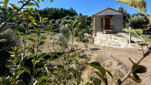 Un pequeño edificio de piedra con una puerta roja y una pared de piedra, rodeado de follaje y árboles.