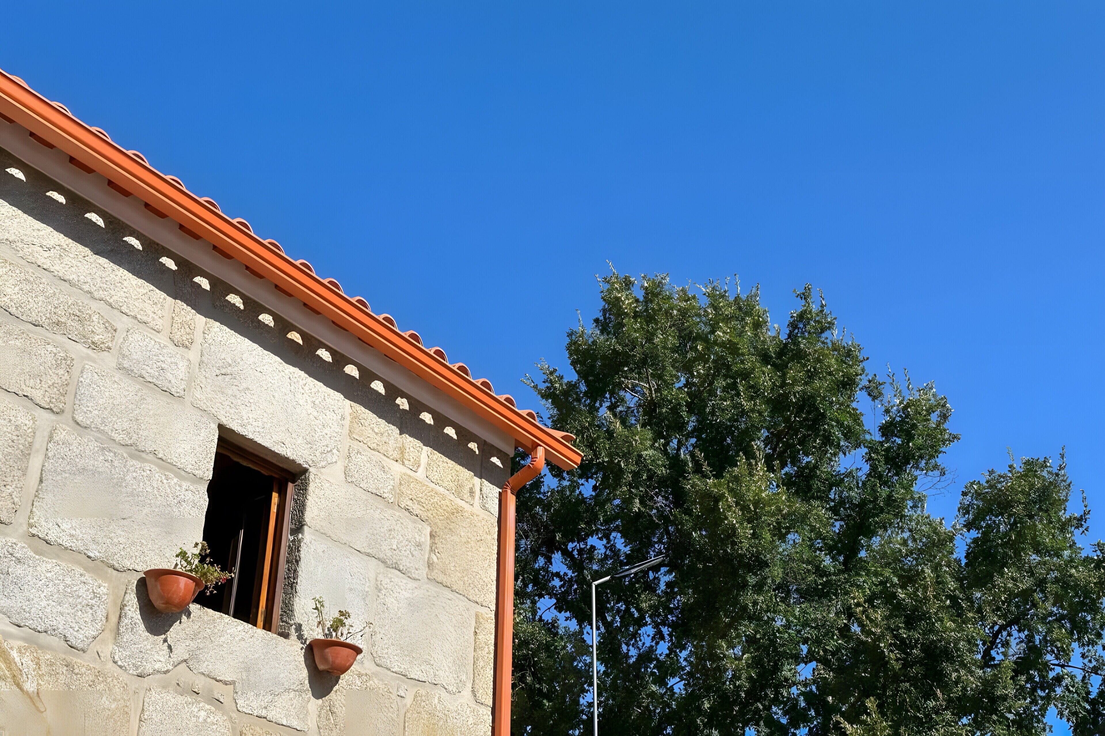 Un edificio in pietra con tetto in tegole, una finestra con una porta e due piante in vaso.