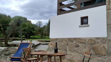 A wooden deck with a pool, a stone wall, and a small window.