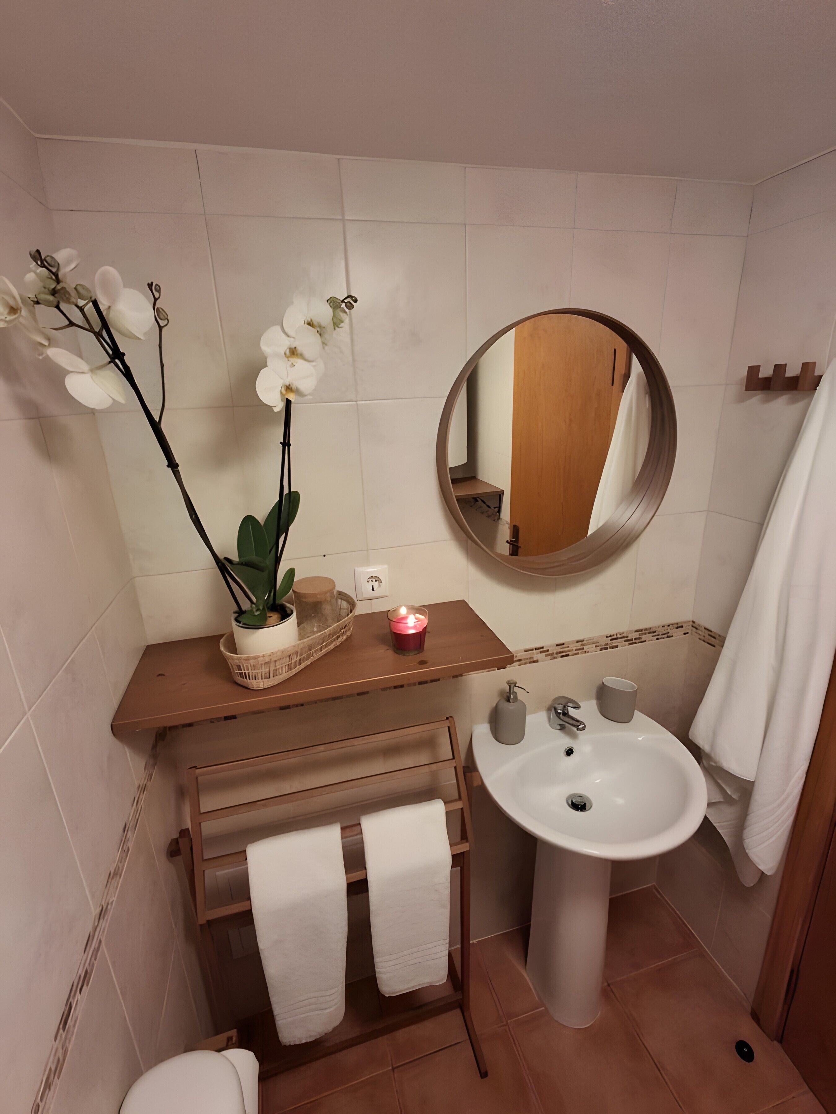 Een badkamer met een houten wastafelmeubel, een witte wasbak, een ronde spiegel en een orchidee.