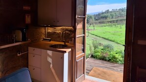Una cocina rústica con un lavamanos, armarios y vistas a un paisaje verde a través de un ventanal abierto.