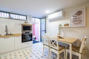 A compact kitchen with white cabinets, a microwave, and an oven. There's a dining table with chairs and a small potted plant. - Apartment 'Almar' with Shared Pool, Wi-Fi and Air Conditioning (Vigo)