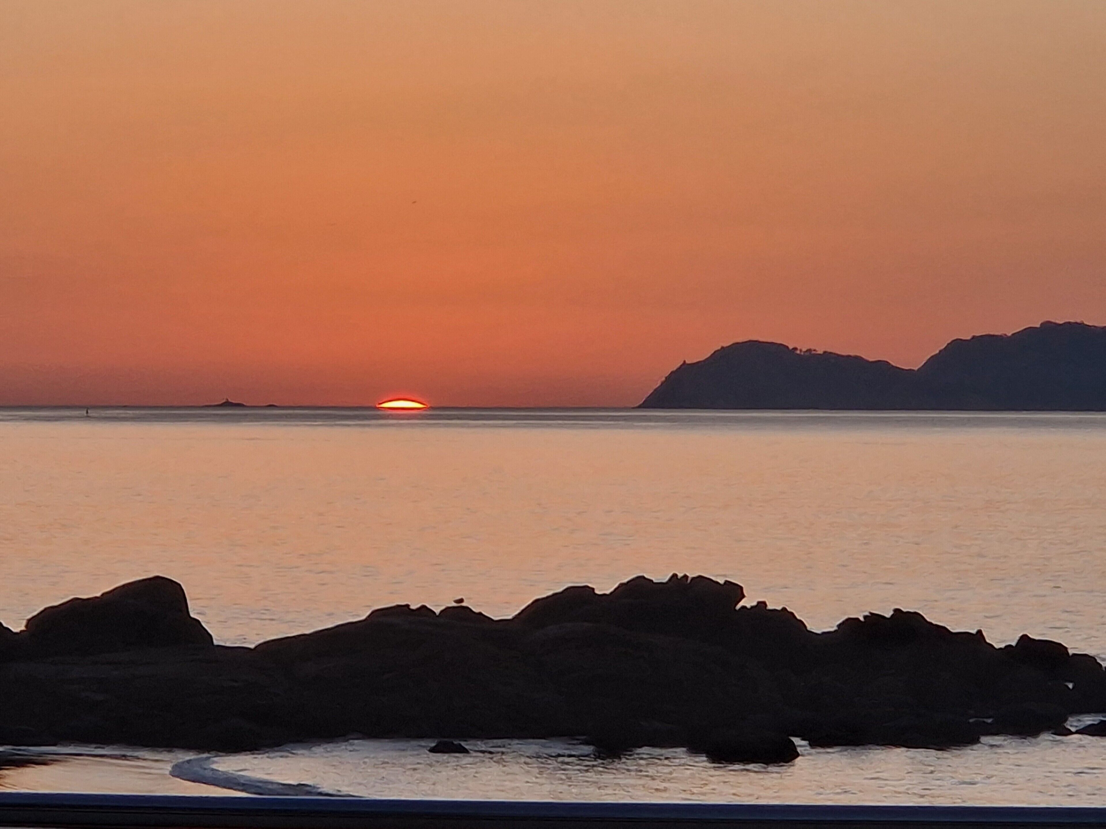 Un capvespre sobre un mar tranquil amb formacions rocoses al primer pla.
