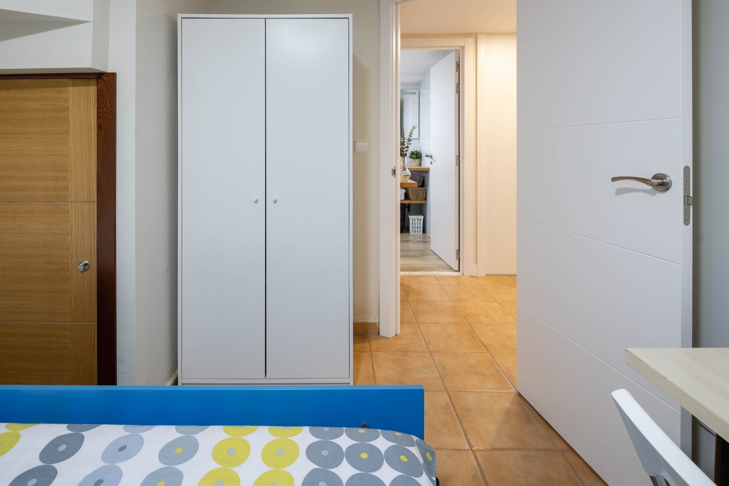 Een slaapkamer met een bed, een kledingkast en uitzicht op een hal met een keukenhoek.