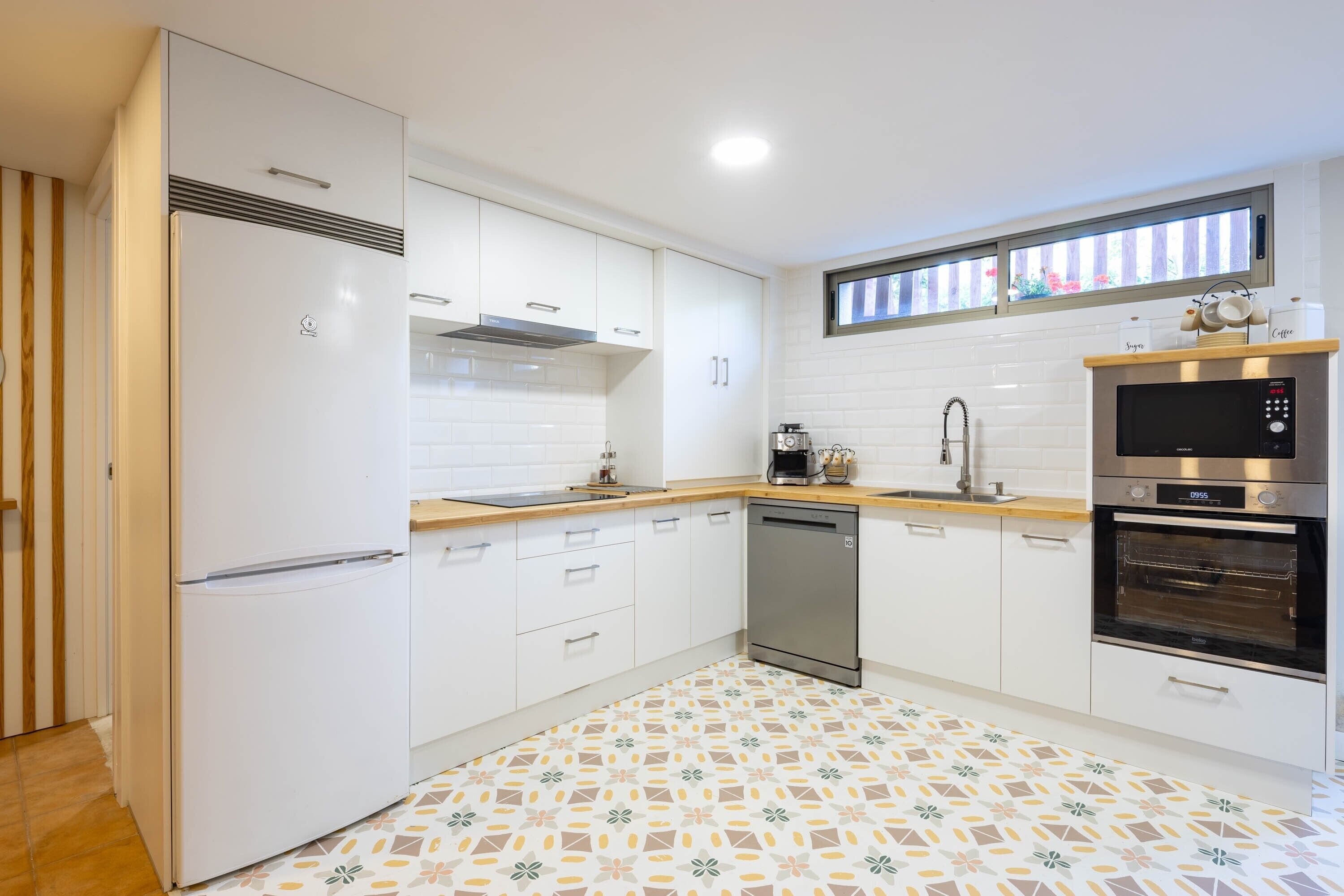 A modern kitchen with white cabinets, stainless steel appliances, a patterned floor, and a window above the sink.