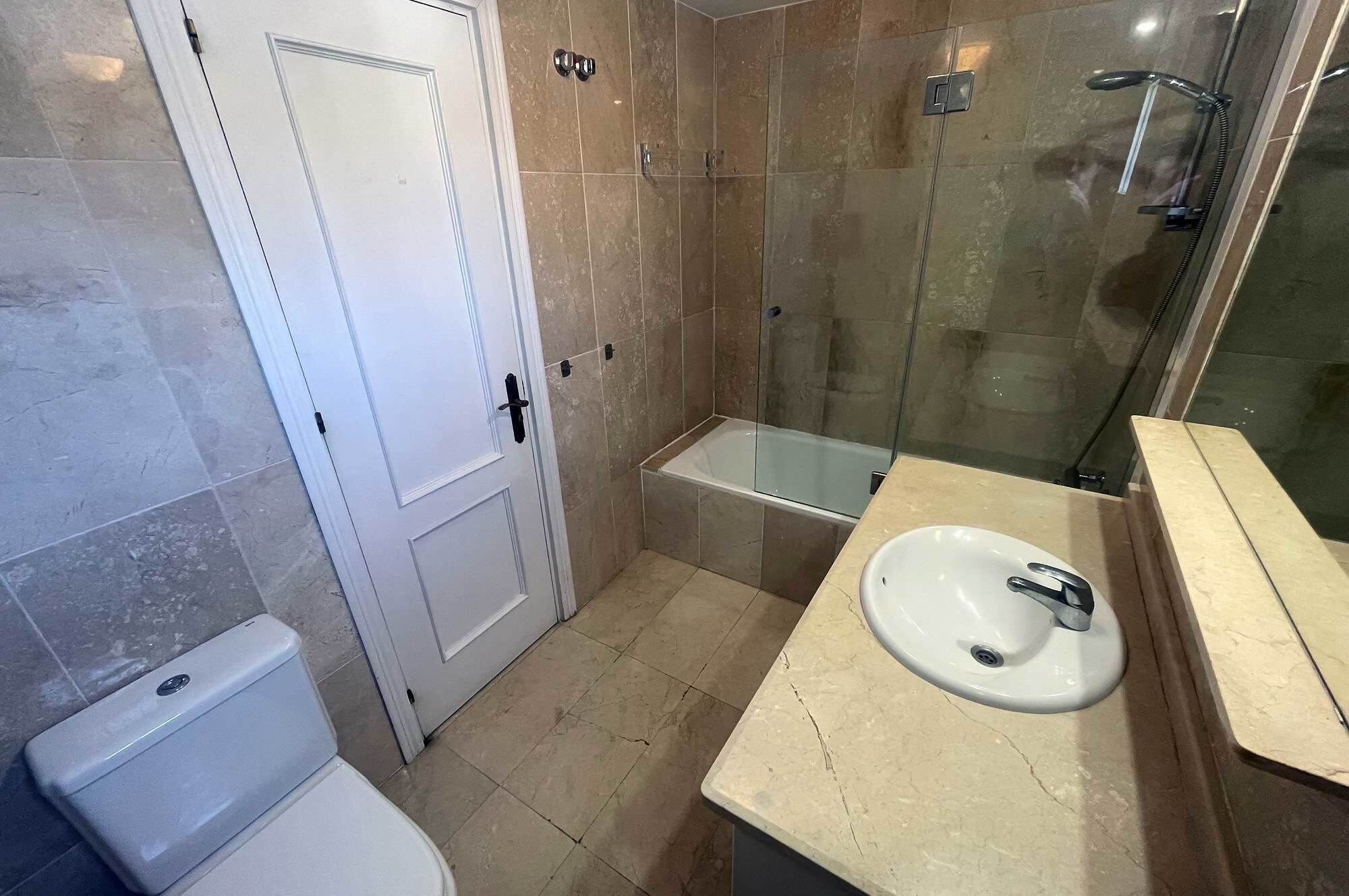 Une salle de bain comprenant des toilettes, une douche fermée par une paroi de verre et un lavabo avec un miroir.