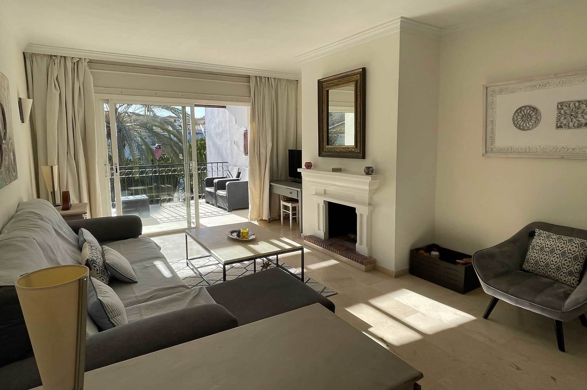 Un salon spacieux comprenant un canapé, une table basse, une cheminée et un balcon agrémenté de rideaux.