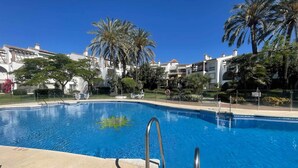 Una piscina con acqua cristallina e blu, circondata da palme e un edificio bianco con balconi.