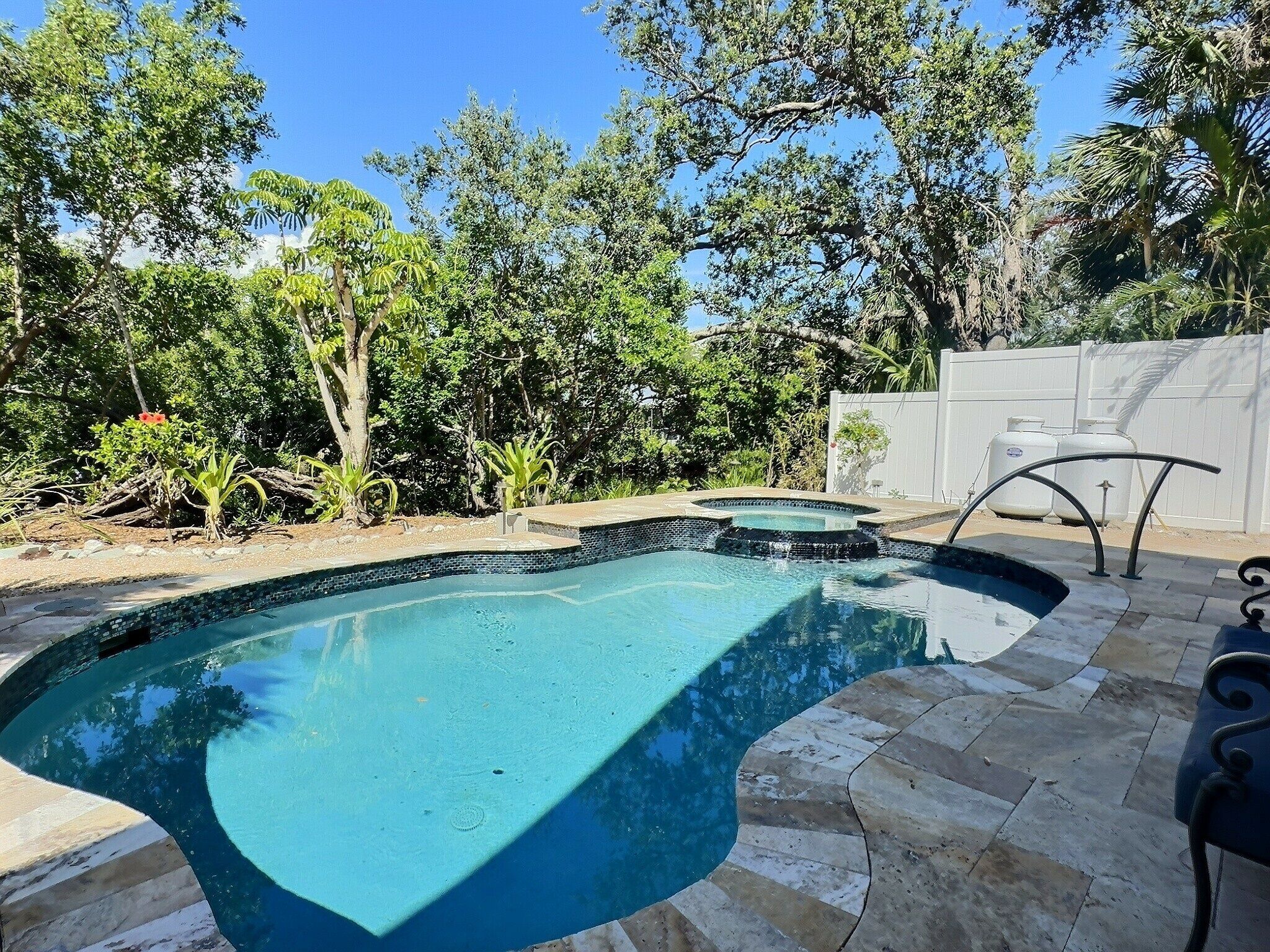 A swimming pool with a curved edge, surrounded by a stone deck and a white fence.