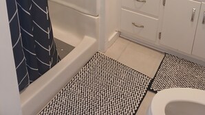 A bathroom with a shower, a sink, a mirror, and patterned floor mats. - Charming 1-bedroom cottage in Holly Pond with AC, WiFi (Holly Pond)