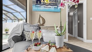 A cozy room with a bed, a dining table with a tray of food and drinks, a potted plant, and a sign for Roelens Vacations. - Privacy, Luxury and Relaxation, Heated Pool & Spa - Villa Courtyard - Roelens (Cape Coral)