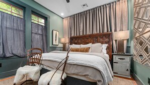 Une chambre à coucher avec un lit en bois, une chaise blanche, une table de chevet et un tapis à motifs.