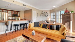 A modern kitchen with stainless steel appliances, a dining area with a yellow sofa and black bar stools, and a bicycle mounted on the wall. - Desert Oasis Apartment at Viera Resort (Henderson)