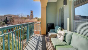 A balcony with a green railing, a wicker sofa with cushions, and a view of a tower in the distance. - Desert Oasis Apartment at Viera Resort (Henderson)