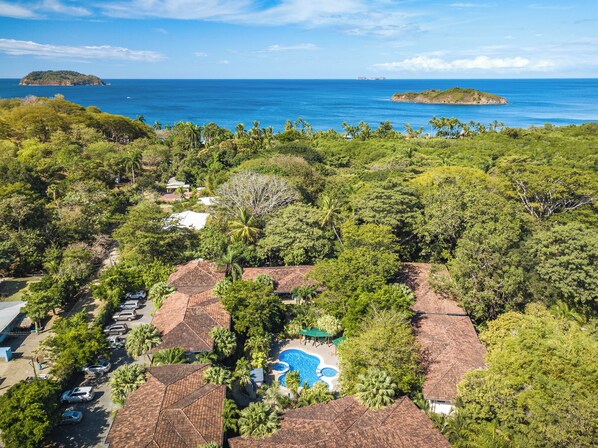 A resort with multiple bungalow-style buildings, a swimming pool, and a view of the ocean and islands.
