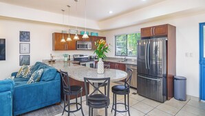A modern kitchen with a central island, stainless steel appliances, and a blue sofa in the living area. - Stylish 1-bedroom condo with workspace, walk to everything + massages on us! (Potrero)