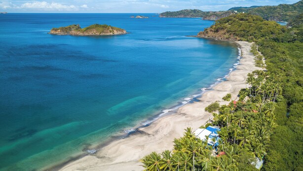 A coastal landscape with a beach, clear blue waters, and lush greenery. - Stylish 1-bedroom condo with workspace, walk to everything + massages on us! (Potrero)