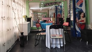 L’intérieur d’un restaurant présente une décoration aux tons verts et blancs, avec un espace repas comprenant des tables et des chaises, un comptoir et un mur décoratif orné de motifs floraux.