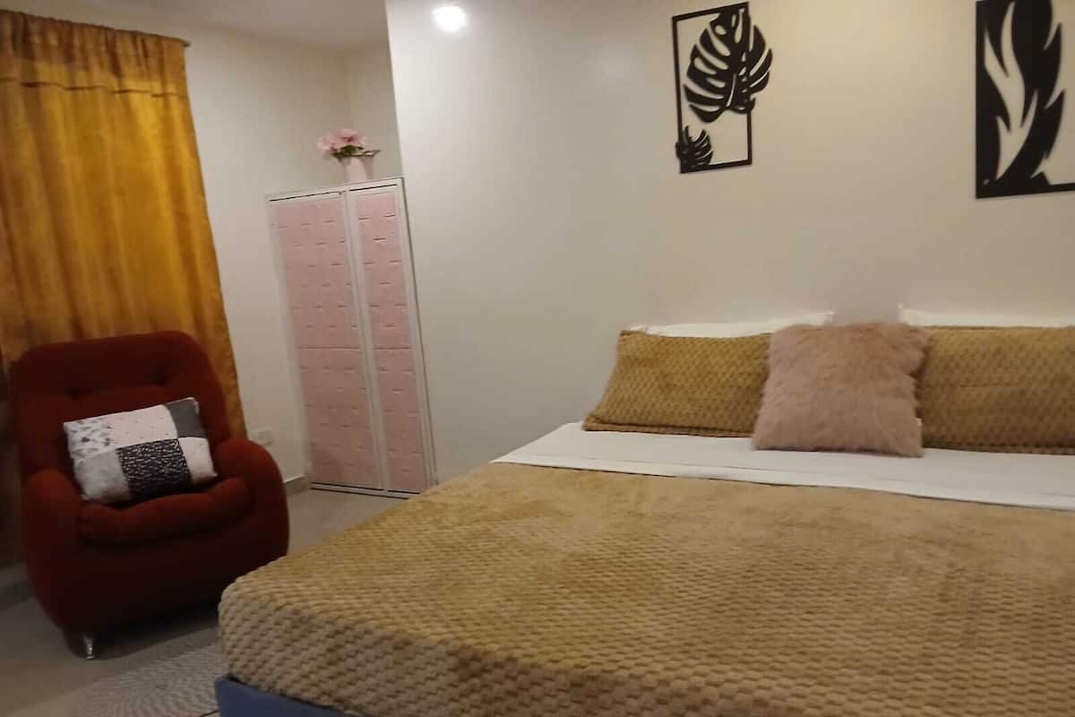 Un dormitorio con cama, un sillón rojo, un armario rosa y decoración en la pared.