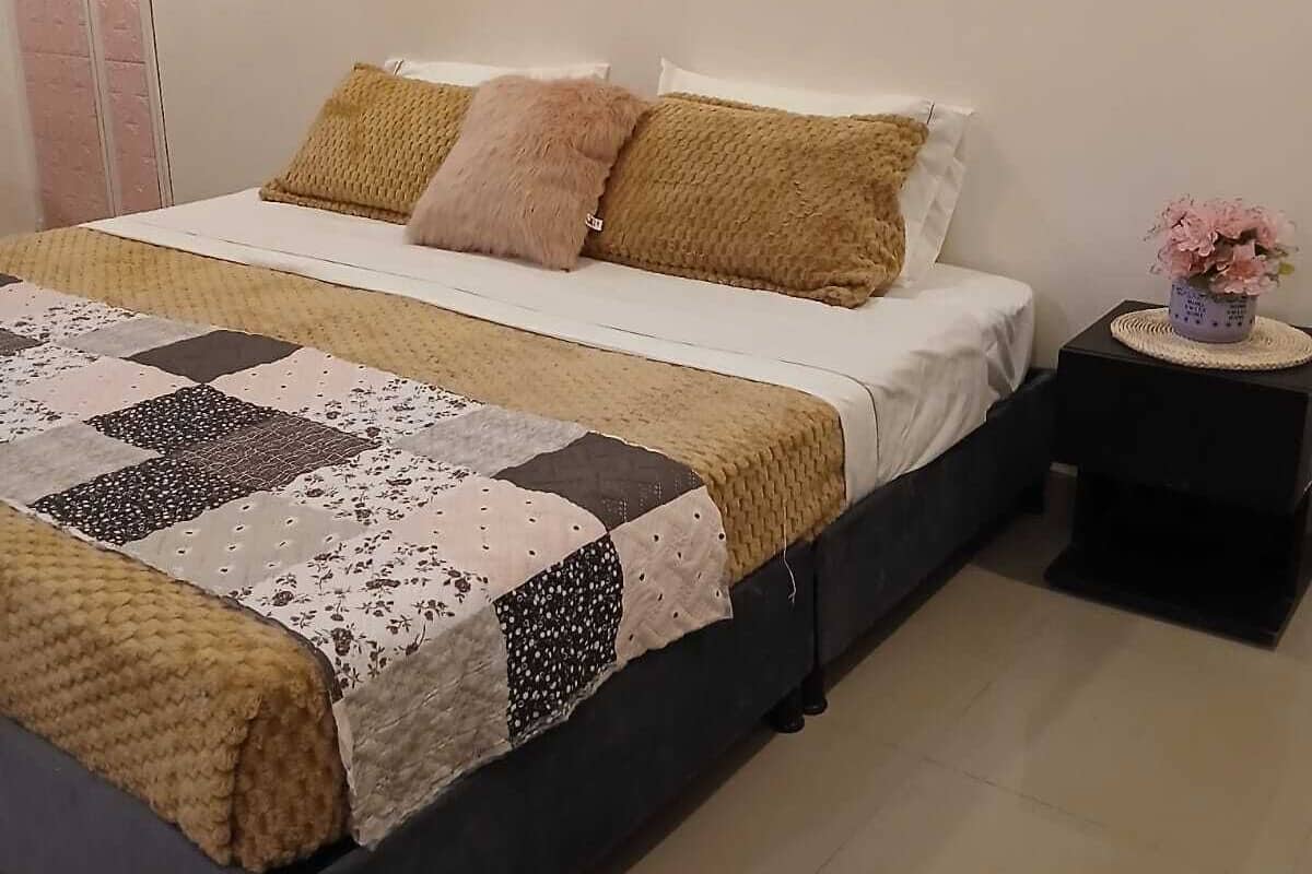 Un dormitorio con cama, almohadas, una mesita de noche y decoración en la pared.