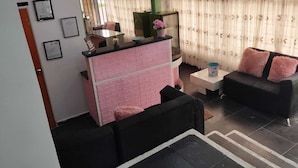 Un salon avec un canapé noir, un comptoir aux motifs en briques roses et une table basse blanche.